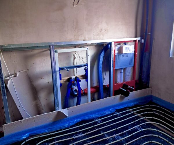 Baustelle mit Rohbau, Monteure installieren Leitungen, Bauleiter mit Tablet.